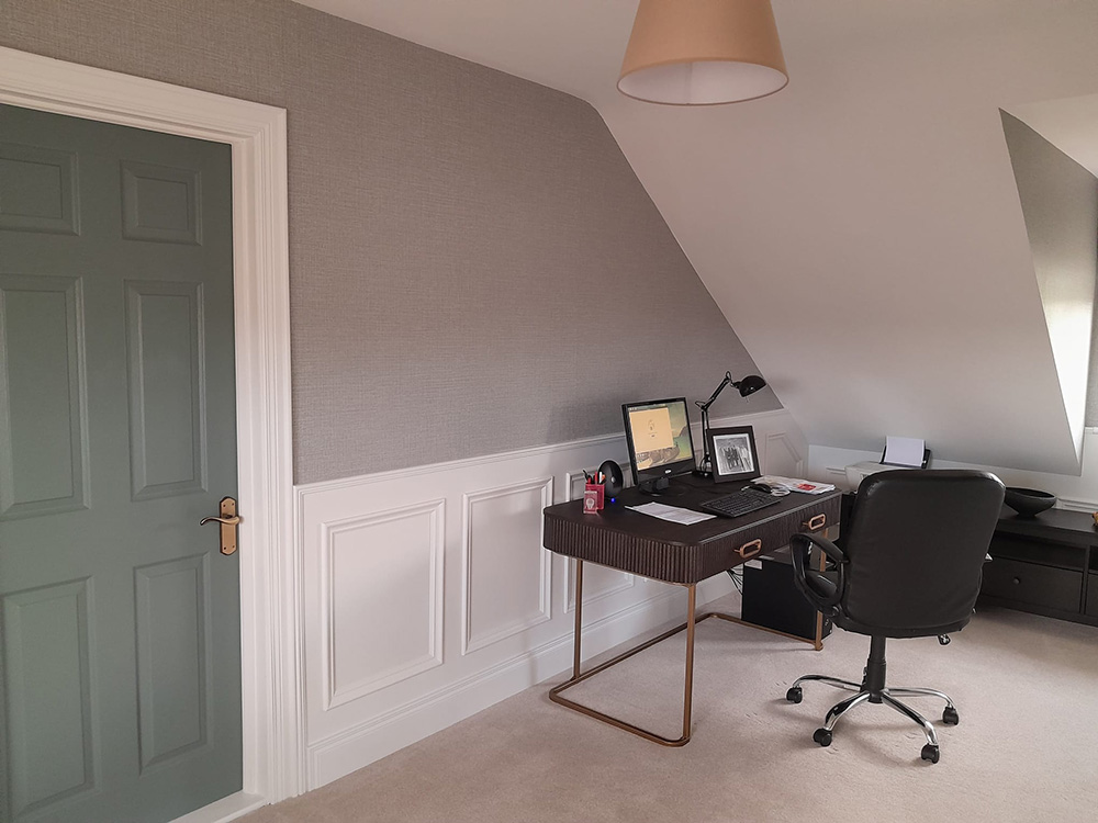 Home office with slated ceiling, white wall panelling and carpet flooring