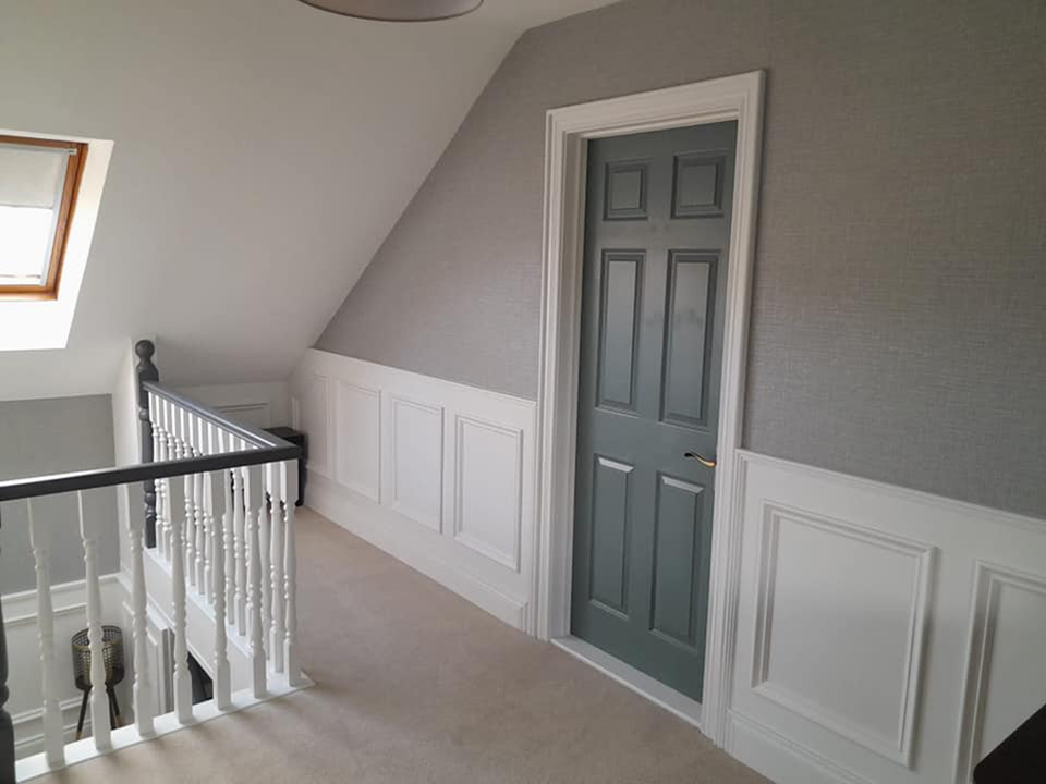 Upstairs hall of a house with white wall panelling and a grey door