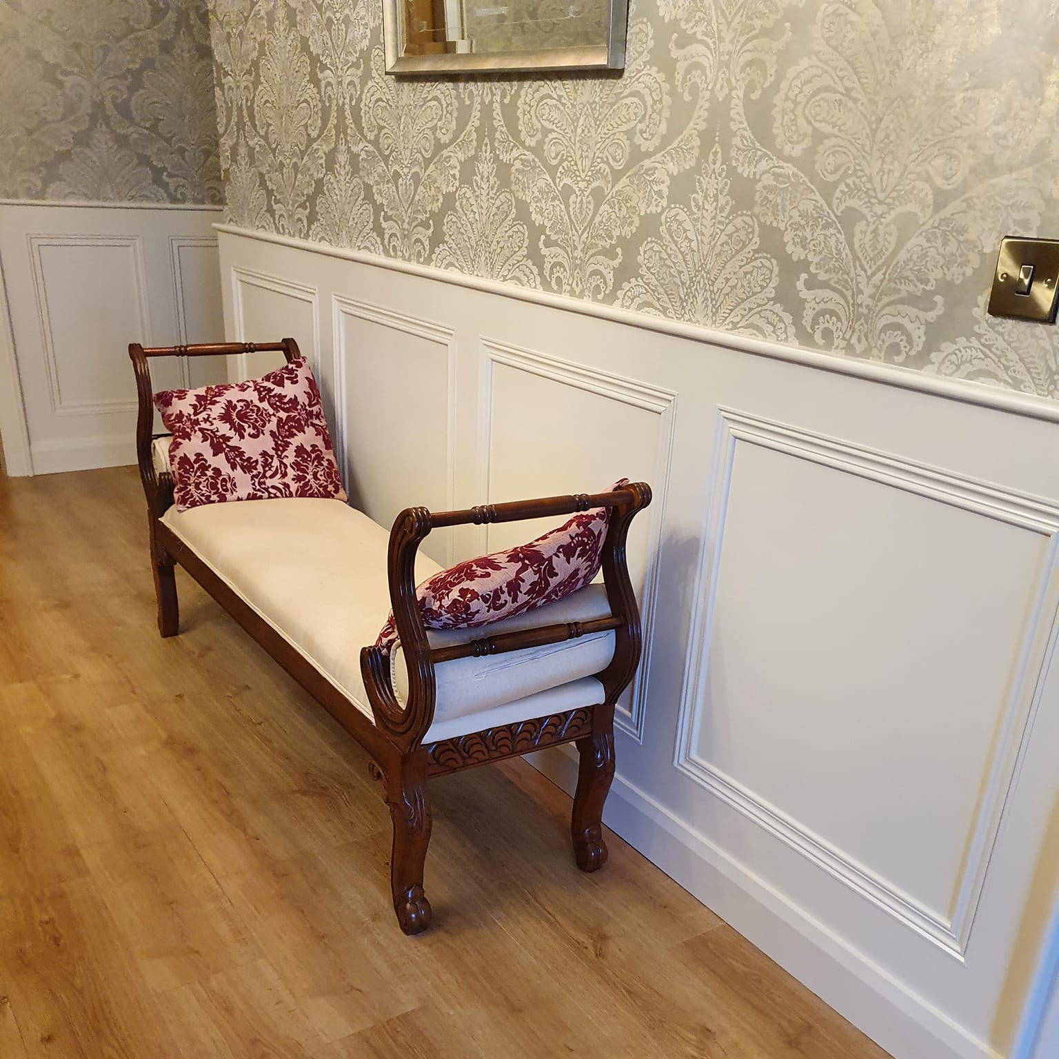 White wall panelling in a hallway with decorative wall paper and a dark wood bench